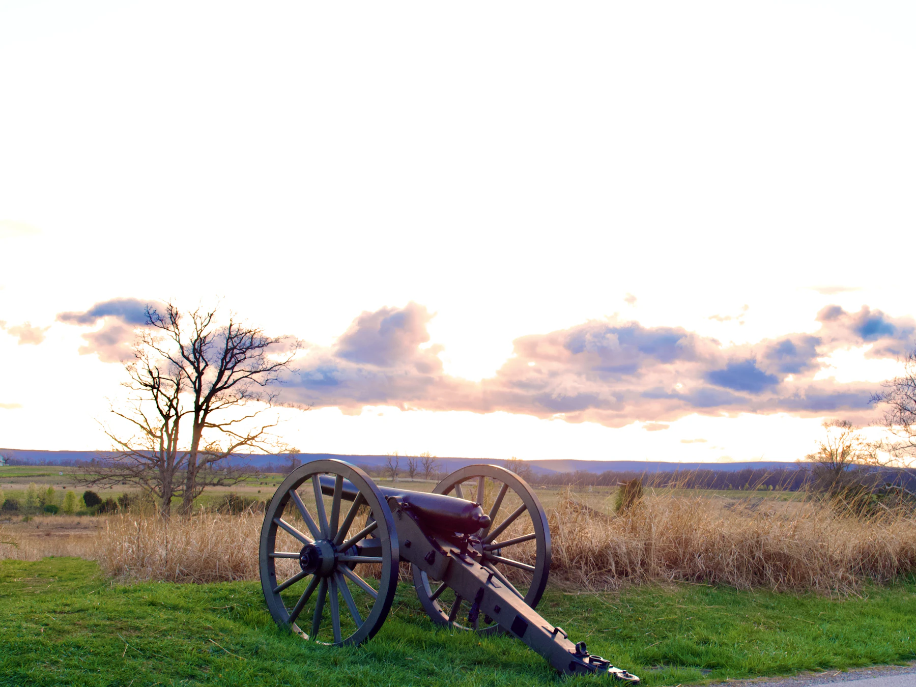 A Civil War cannon on a grassy field at dusk, with bare trees and low hills behind it