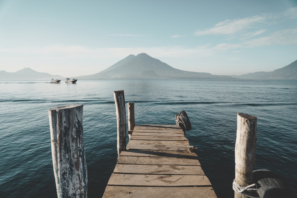 a dock leading out to a body of water with boats in it with Lake Atitlán in the background
