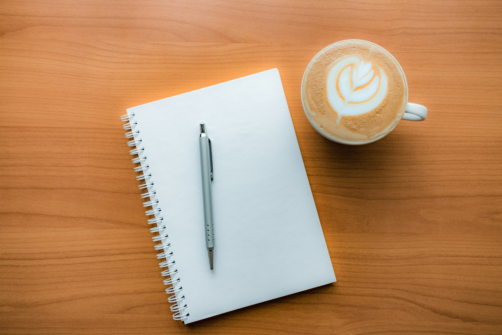 Caderno aberto com caneta ao lado de uma xícara de café
