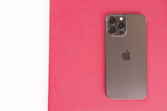 A modern smartphone with a sleek design and multiple camera lenses is placed on a red surface. The phone's back is metallic and features a prominent brand logo.