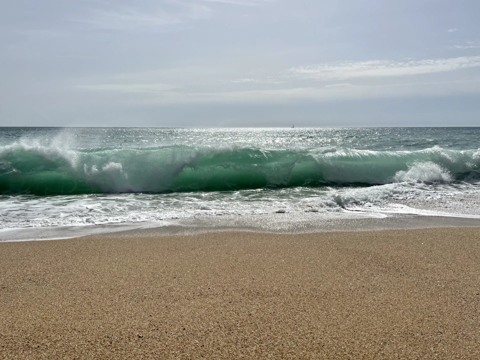 Large, light green wave crashes onto the shore with breaking white foam