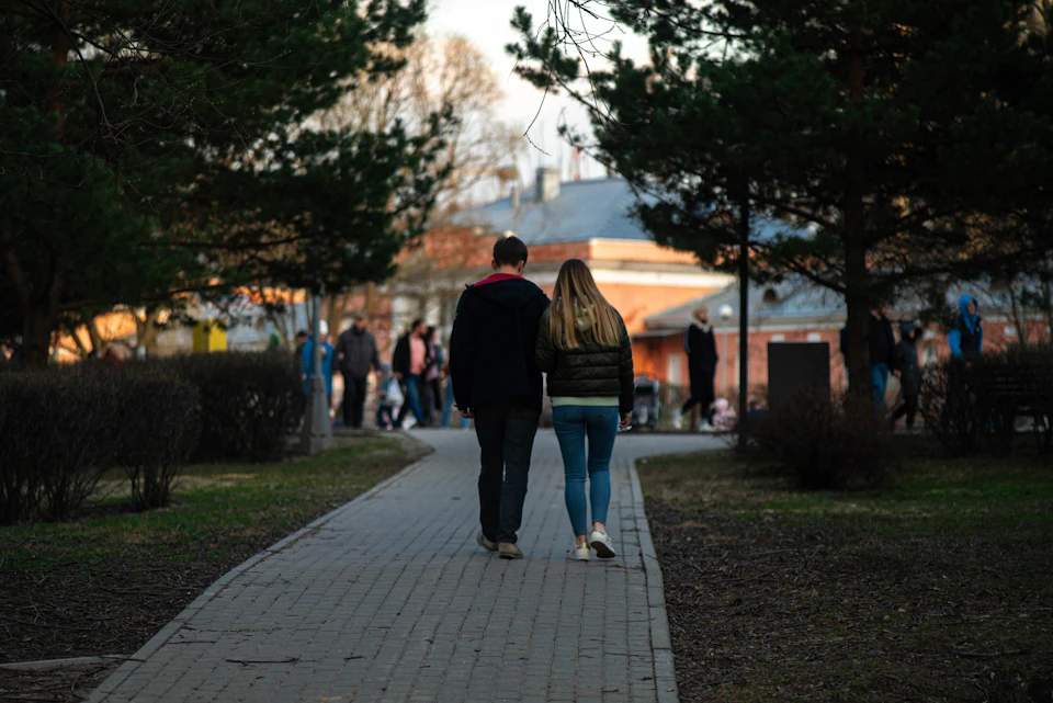 Couple walking hand-in-hand on brick path through lush greenery and trees in park