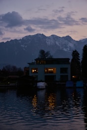 Cozy evening scene of a lakeside home glowing warmly with lights reflecting on calm water.