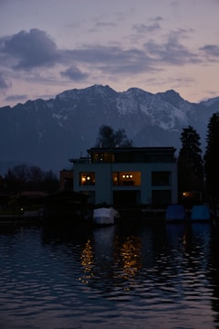 Cozy evening scene of a lakeside home glowing warmly with lights reflecting on calm water.