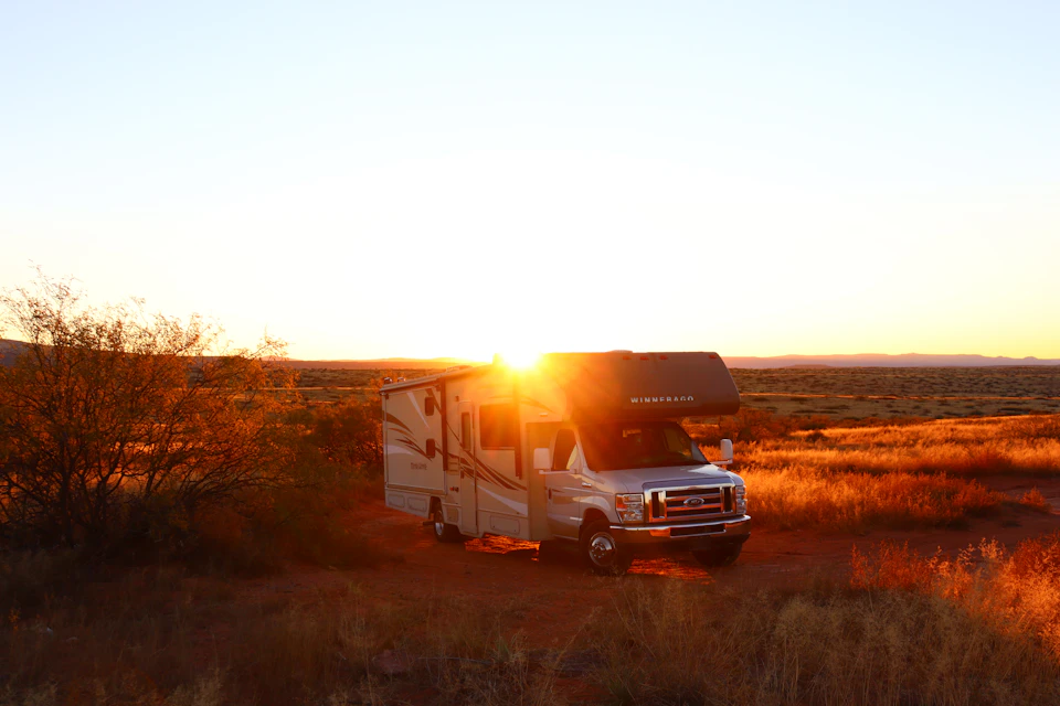 White and gray camper van parked on a dirt road with sunset in background