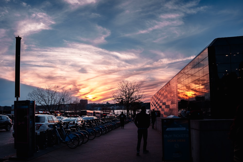 a group of people walking on a sidewalk next to a building with a sunset