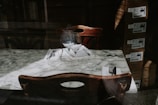 An elegant marble table set for two with wine glasses and utensils rests against a dark wooden backdrop. Boxes are stacked in the corner, adding an industrial element to an otherwise refined ambiance.