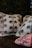 Four pillows featuring embroidered floral patterns are placed together. Two of the pillows have intricate designs with blue and red flowers, while one has a red and white striped pattern. The background is dark, making the pillows stand out.