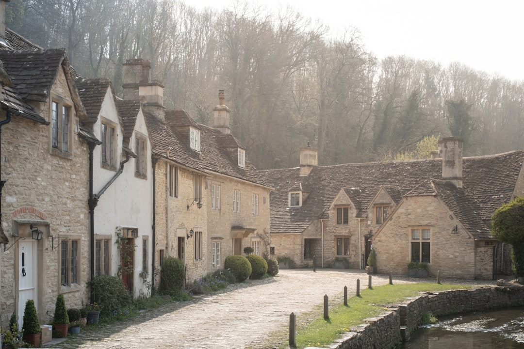 Stone cottages by the river with forest behind in the Cotswolds Village of Castle Combe, North Wiltshire, UK –  Photo by Yaopey Yong | Castle Combe England