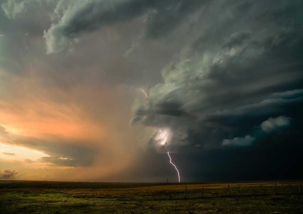 a field with a fence and a cloudy sky with lightning