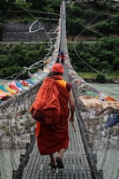 Monk crosses a serene river in Bhutan as colorful Buddhist prayer flags flutter in the wind