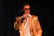 Jai Reign performing live on stage with gold accents glowing in the background.