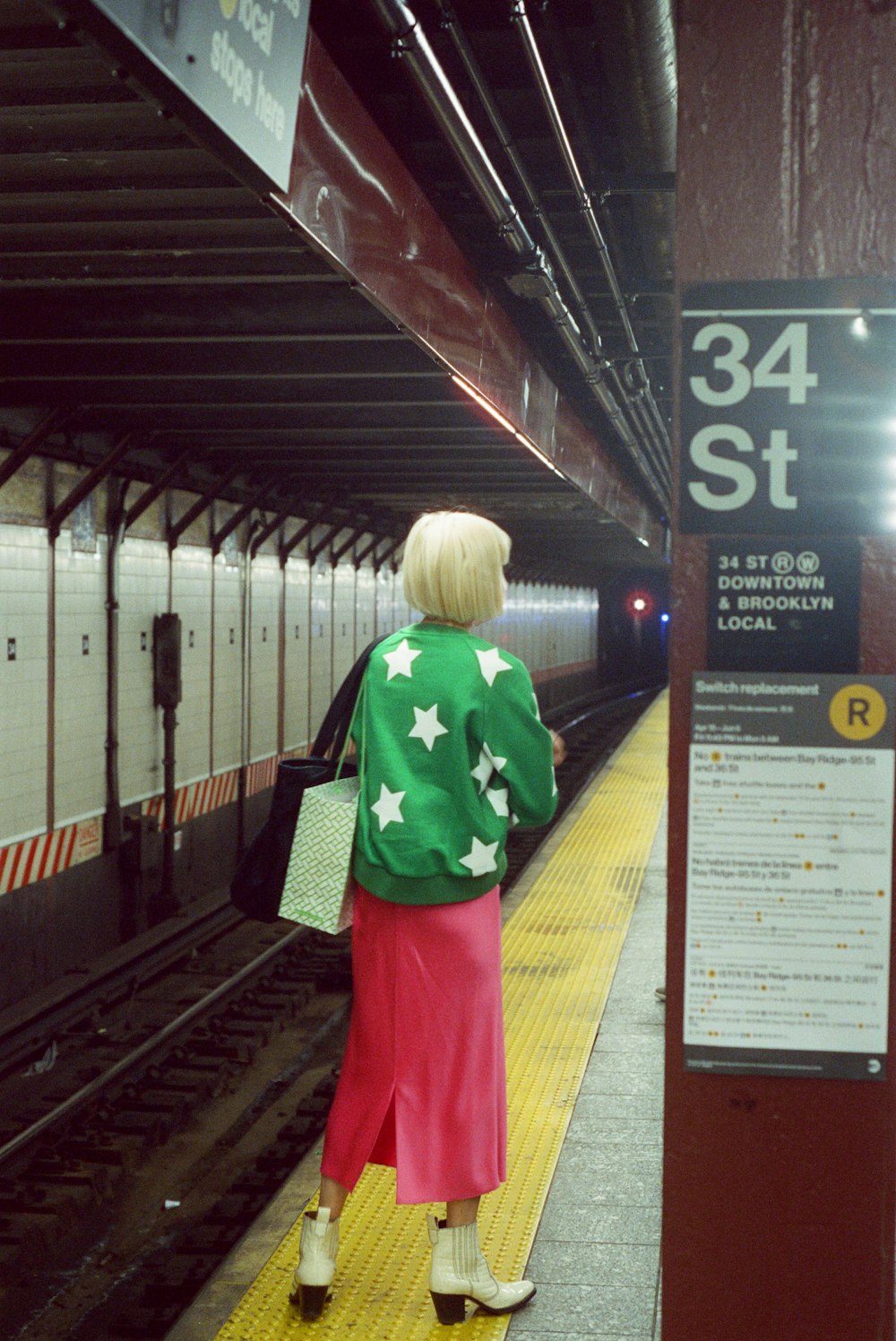 uma pessoa em uma jaqueta verde e saia vermelha em pé em uma plataforma