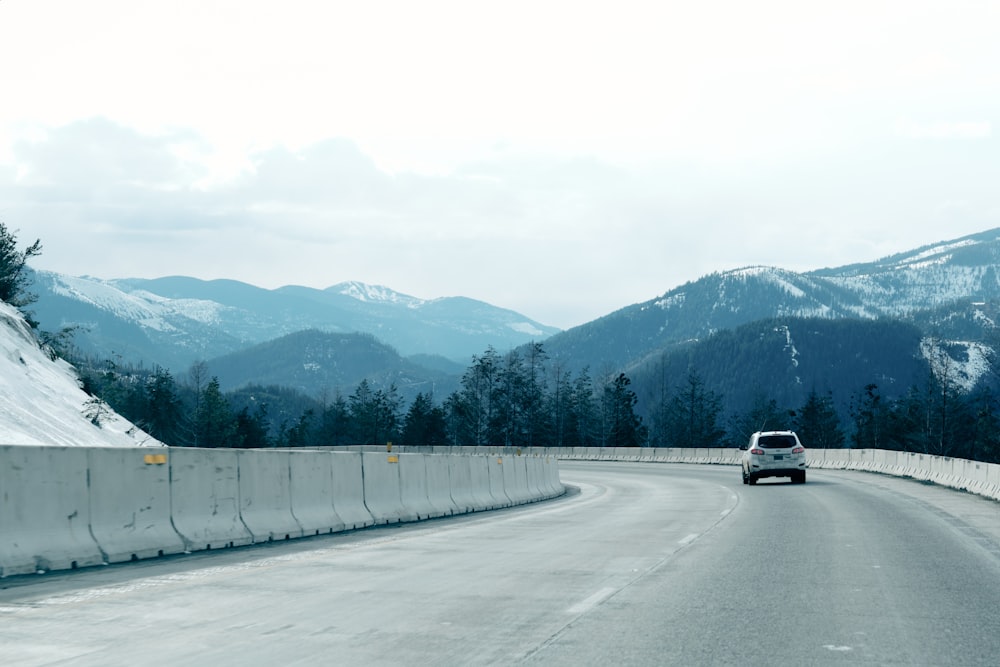 a car driving on a road with snow covered mountains in the background