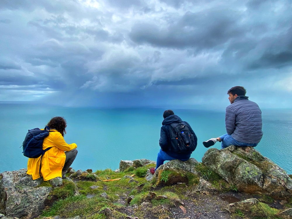 a man and woman sitting on a rock overlooking the ocean