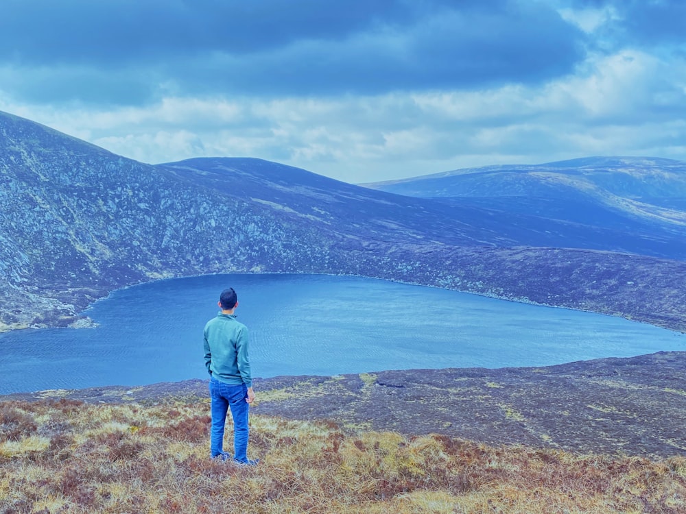 um homem de pé em uma colina com vista para um corpo de água