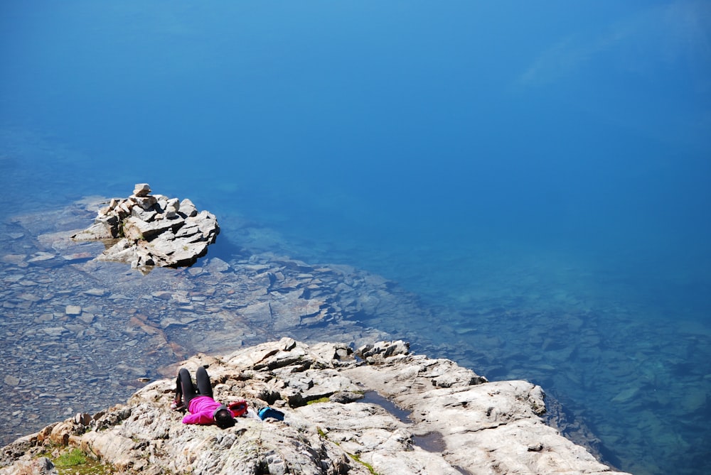 a person lying on a rocky hill by the water