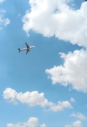 An airplane soaring above fluffy clouds on a clear blue sky.