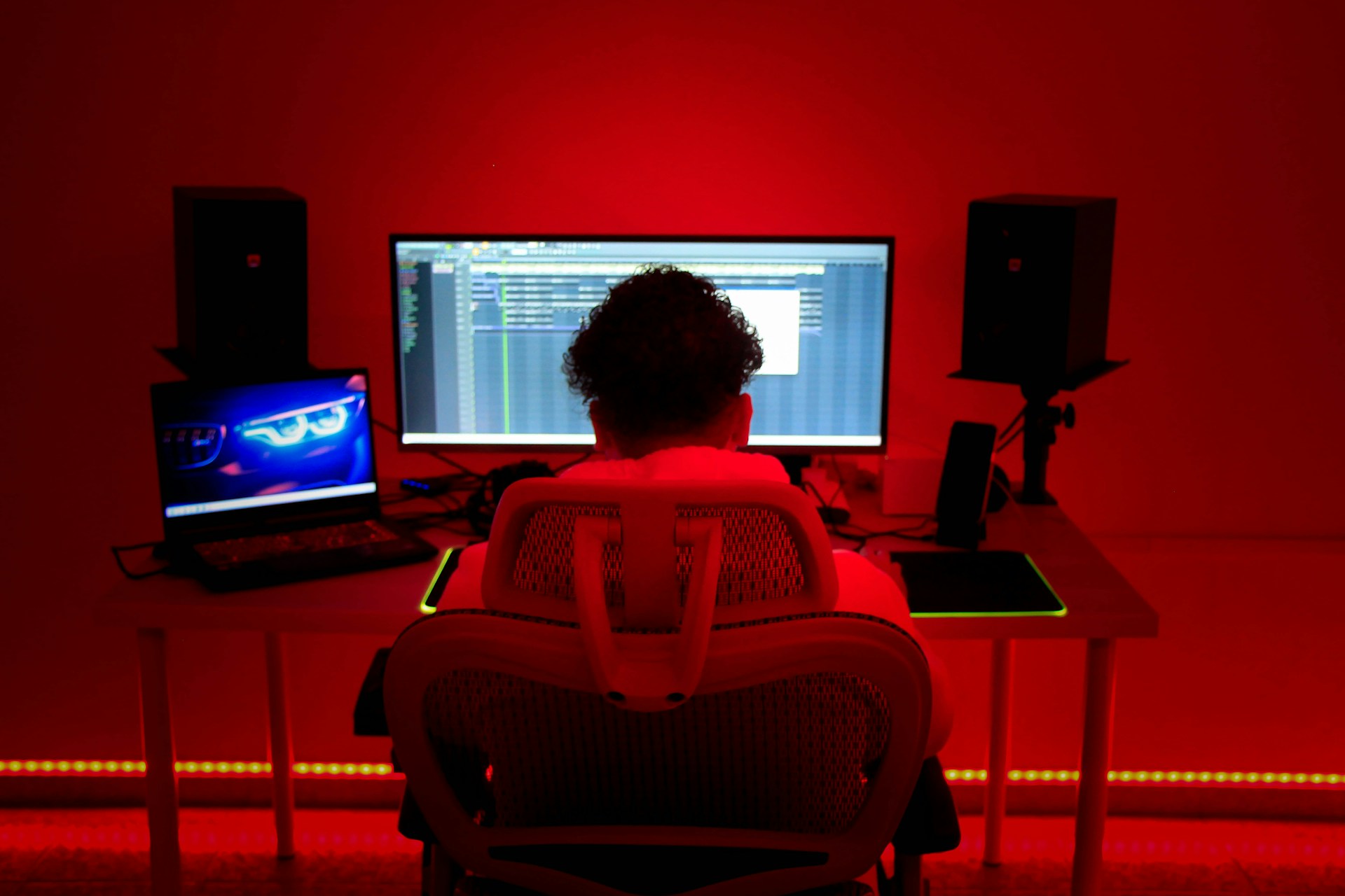 a person sitting in a chair in front of a red wall with a laptop and speakers