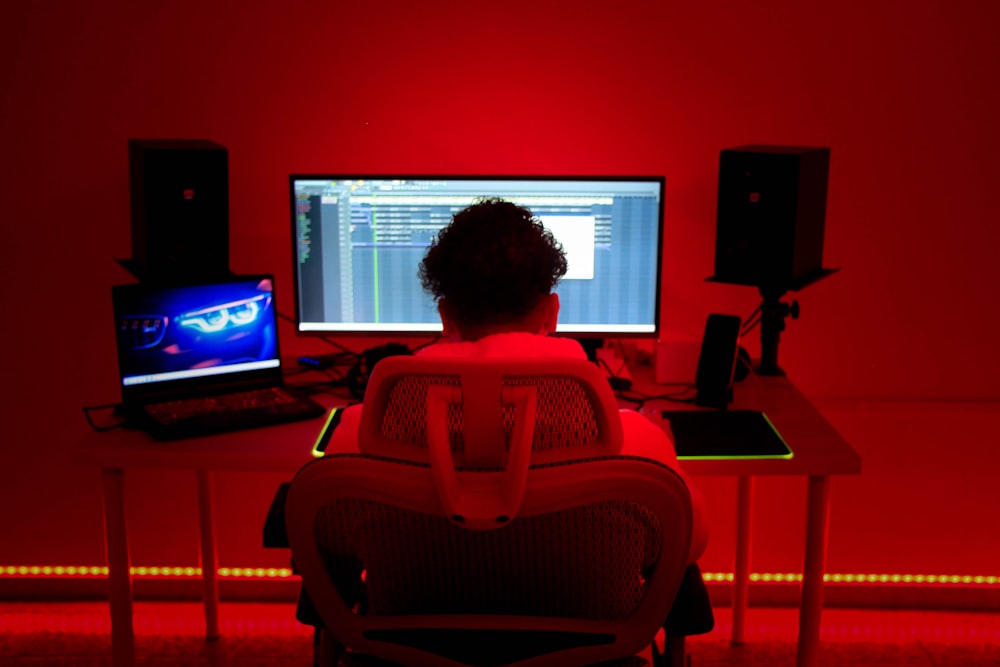 a person sitting in a chair in front of a red wall with a laptop and speakers