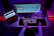 A focused young professional working late at a sleek desk with dual monitors displaying cloud infrastructure diagrams under neon blue lighting.
