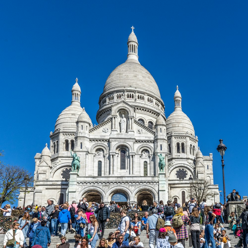 a large crowd of people outside of a large white building with Sacré-Cœur, Paris in the background
