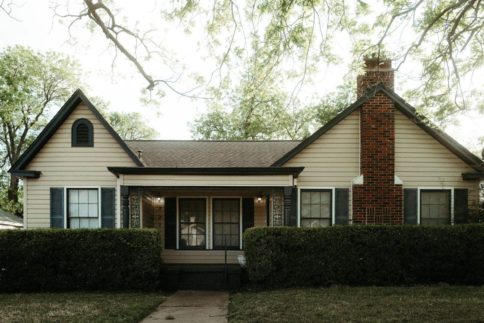 A traditional single-story home with a prominent brick chimney and mature shrubs