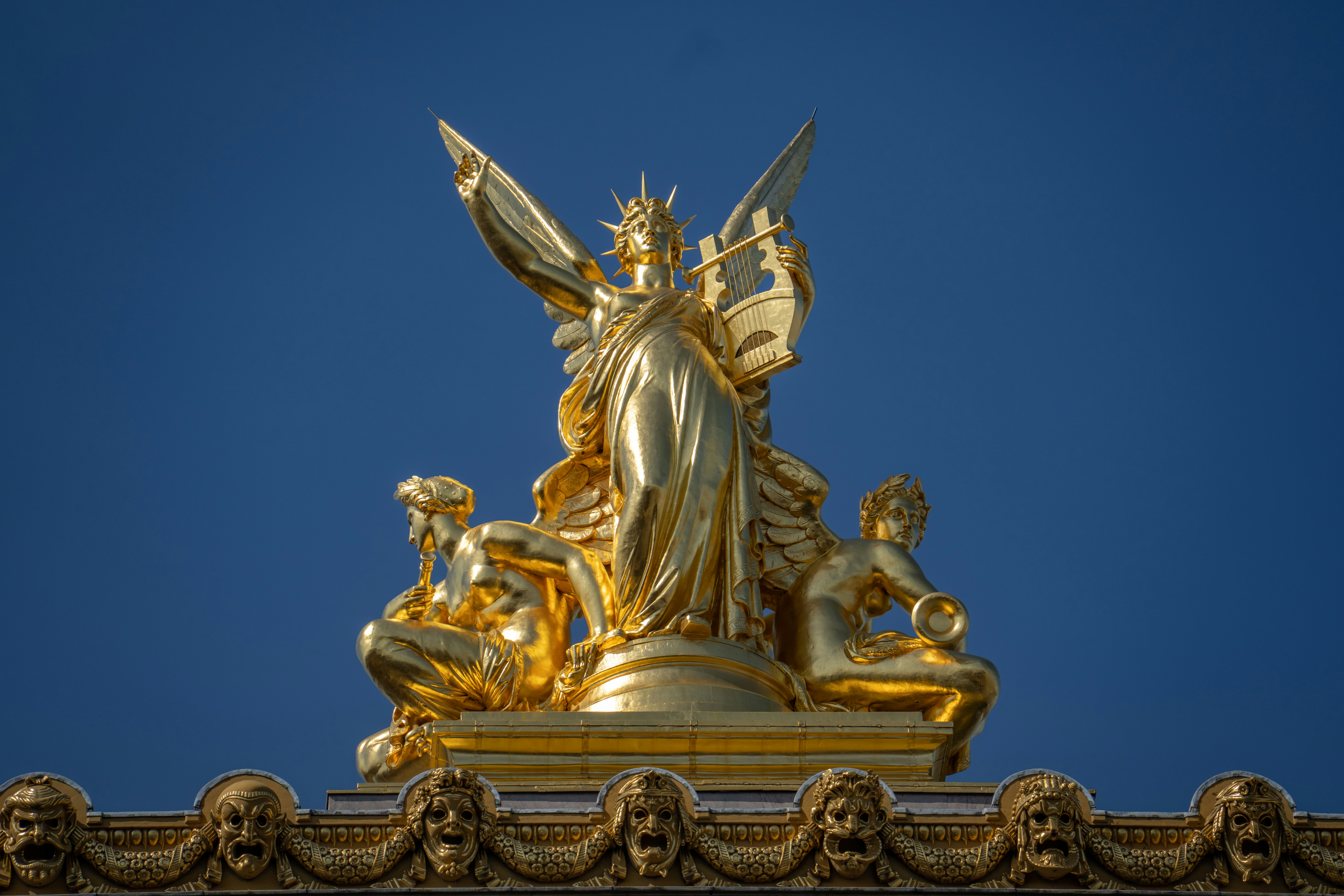 a golden statue of a woman and a man on a throne with Palais Garnier in the background