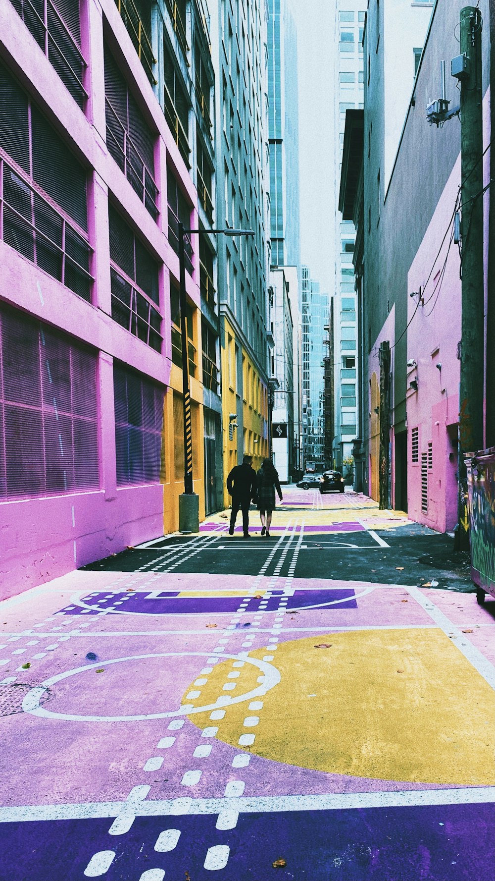 a couple people walking down a street between buildings