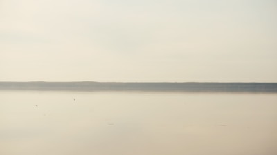 A minimalist landscape with soft pastel skies and calm waters reflecting the horizon.