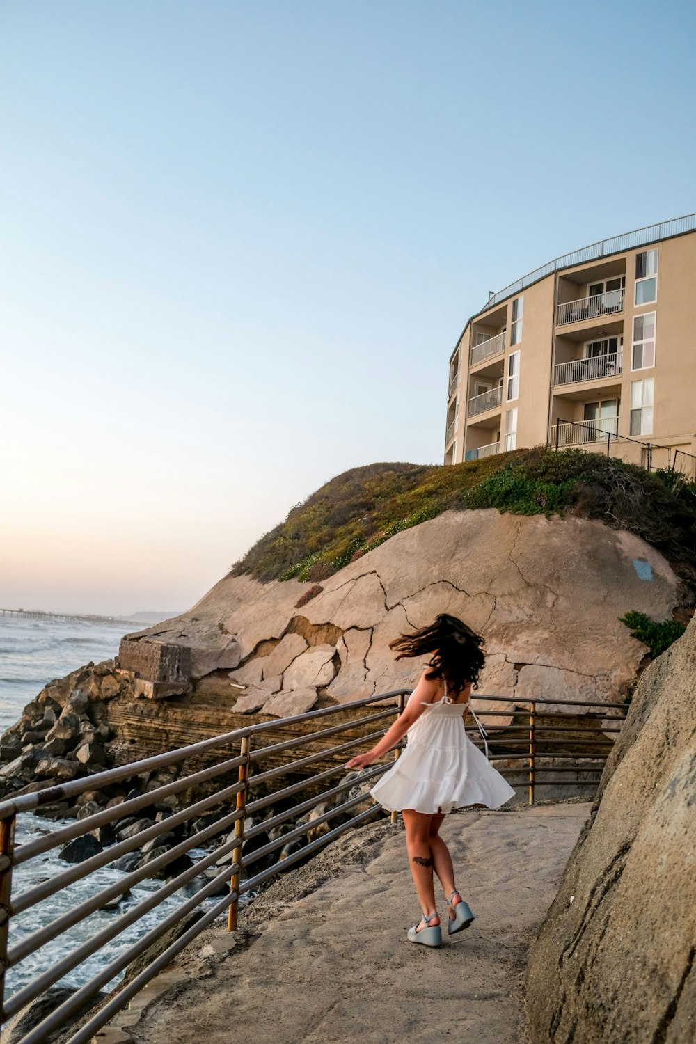 a person walking on a path by a cliff and a building