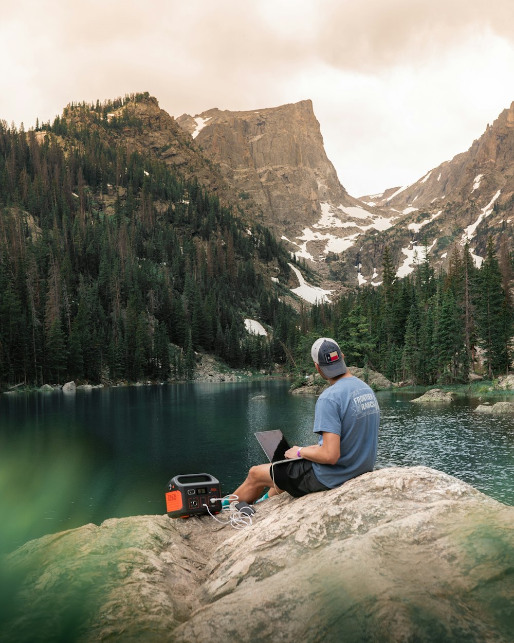 a man sitting on a rock by a lake with a laptop