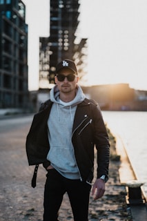 Urban young man wearing a sleek black jacket from El Abem, walking confidently through a city street at dusk.