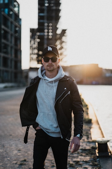 Urban young man wearing a sleek black jacket from El Abem, walking confidently through a city street at dusk.