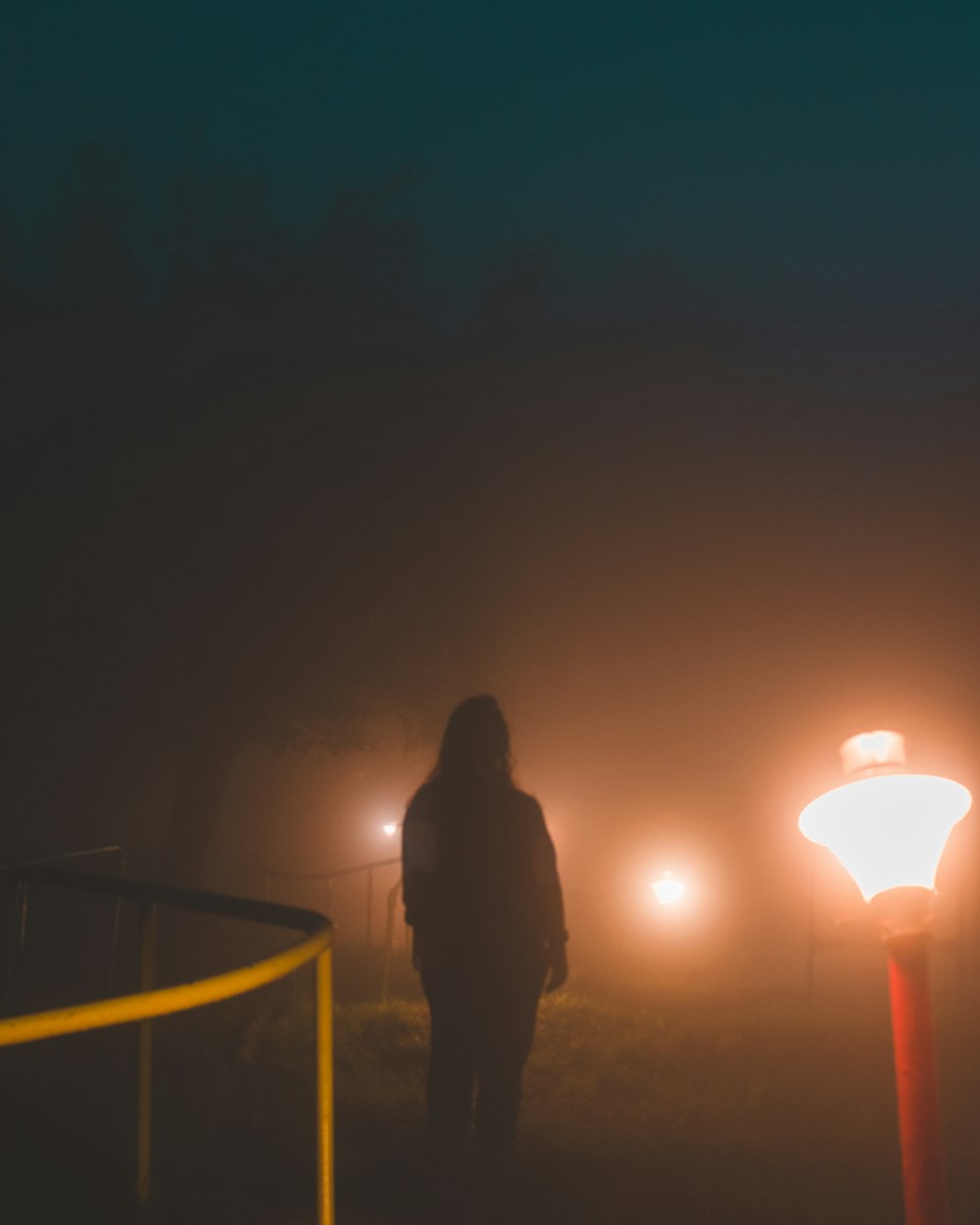 a person standing in a foggy area with street lights