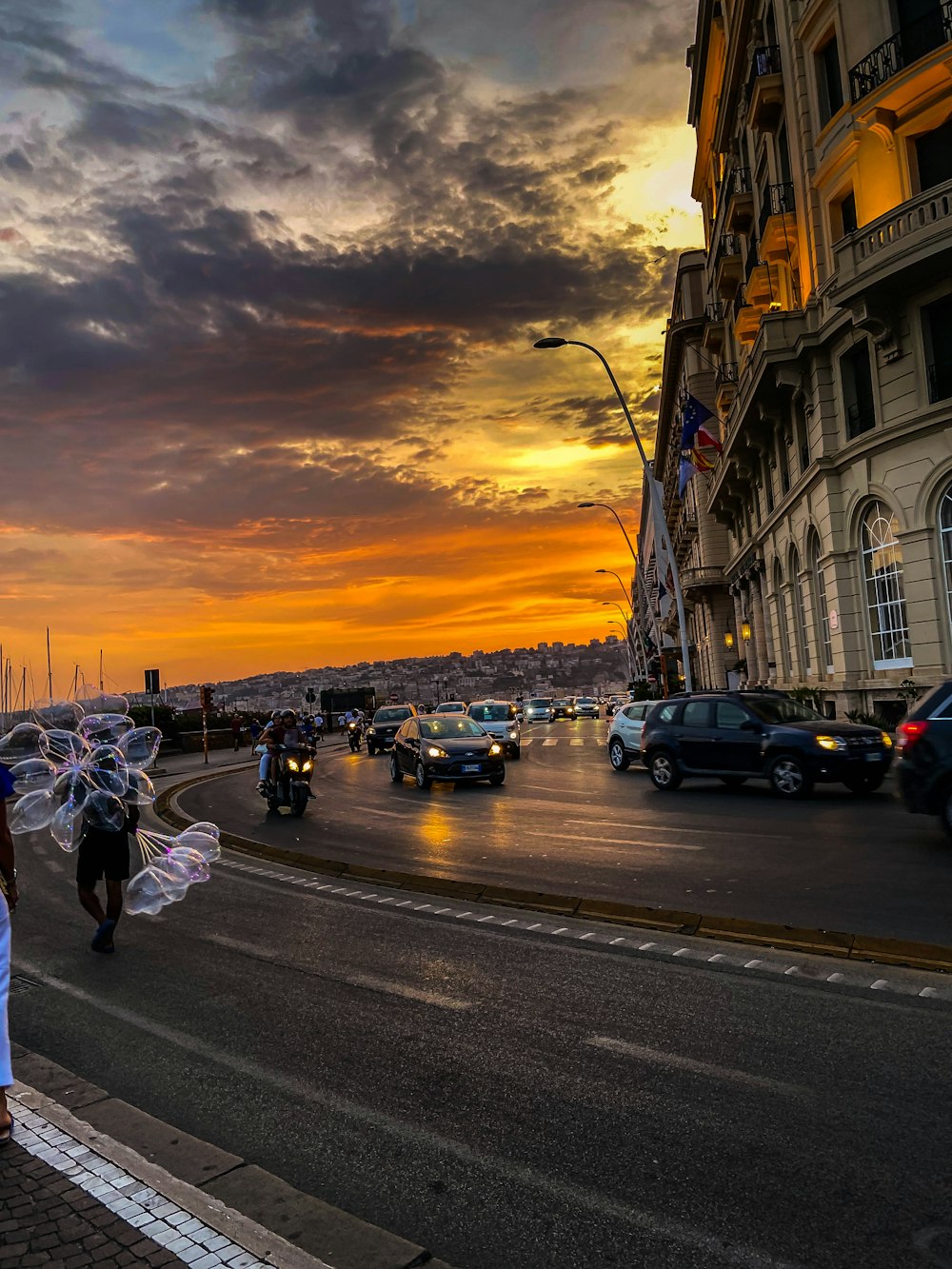 a street with cars and people on it with a sunset in the background