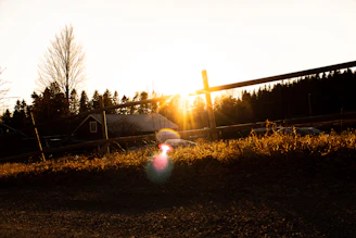 A warm sunset over rolling farmland with a rustic wooden fence in the foreground.