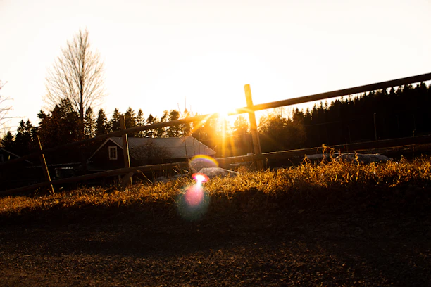 A warm sunset over rolling farmland with a rustic wooden fence in the foreground.