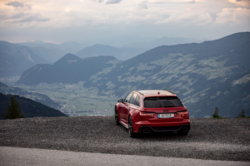 a red car on a road with mountains in the background