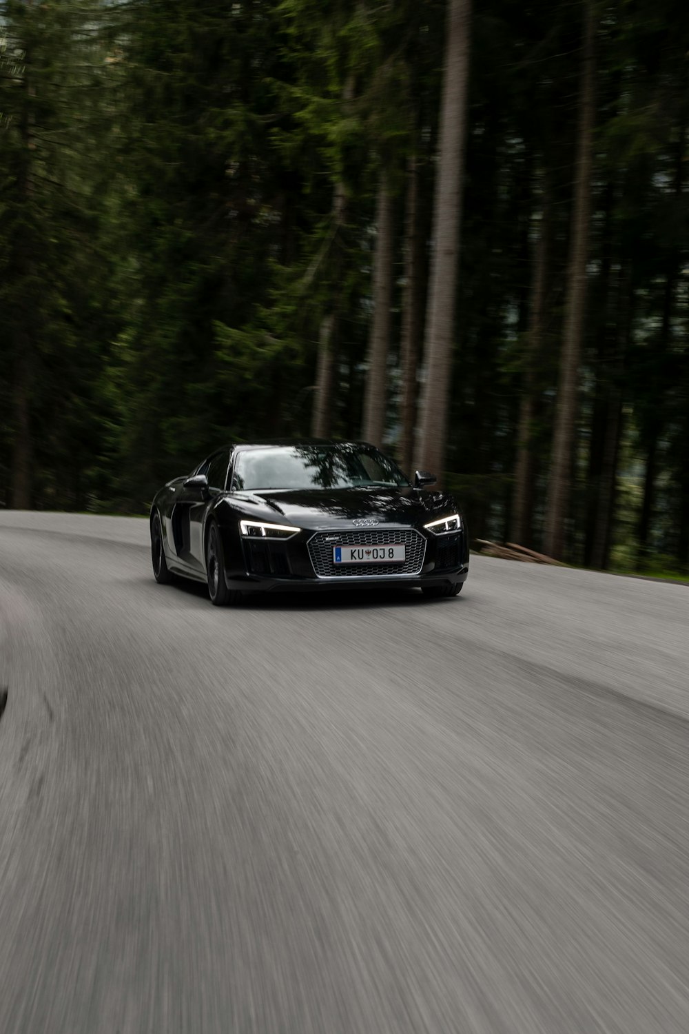 a black car on a road with trees on either side of it