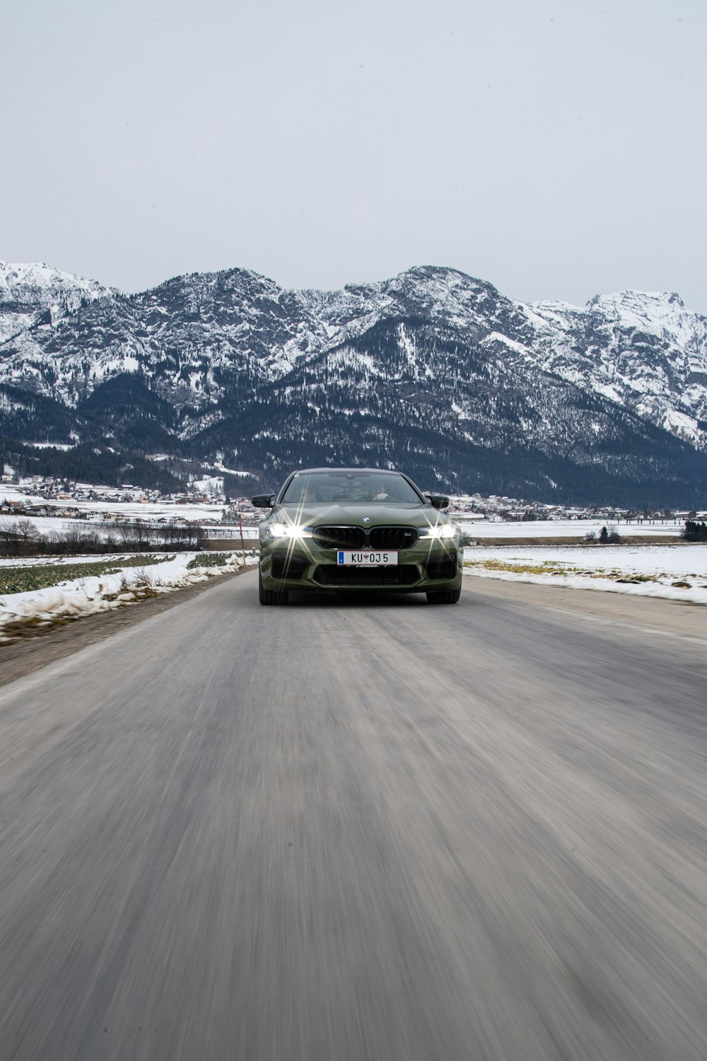 a car driving on a road with snow covered mountains in the background