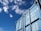 A blue shipping container is positioned against a bright blue sky with scattered clouds. The container has visible numbers and text printed in white on its surface, including weight specifications.