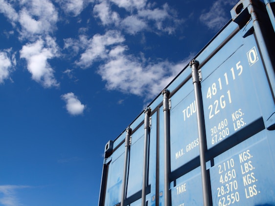 A rugged 40-foot high cube shipping container painted bright blue standing securely on a concrete lot under a clear sky.