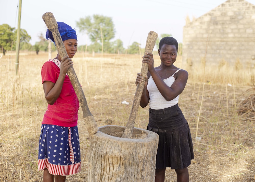 a couple of women holding a wooden pole in a field