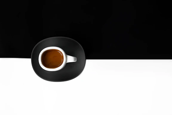 A beautifully styled cup of espresso on a minimalist black and white table with green cedar accents.