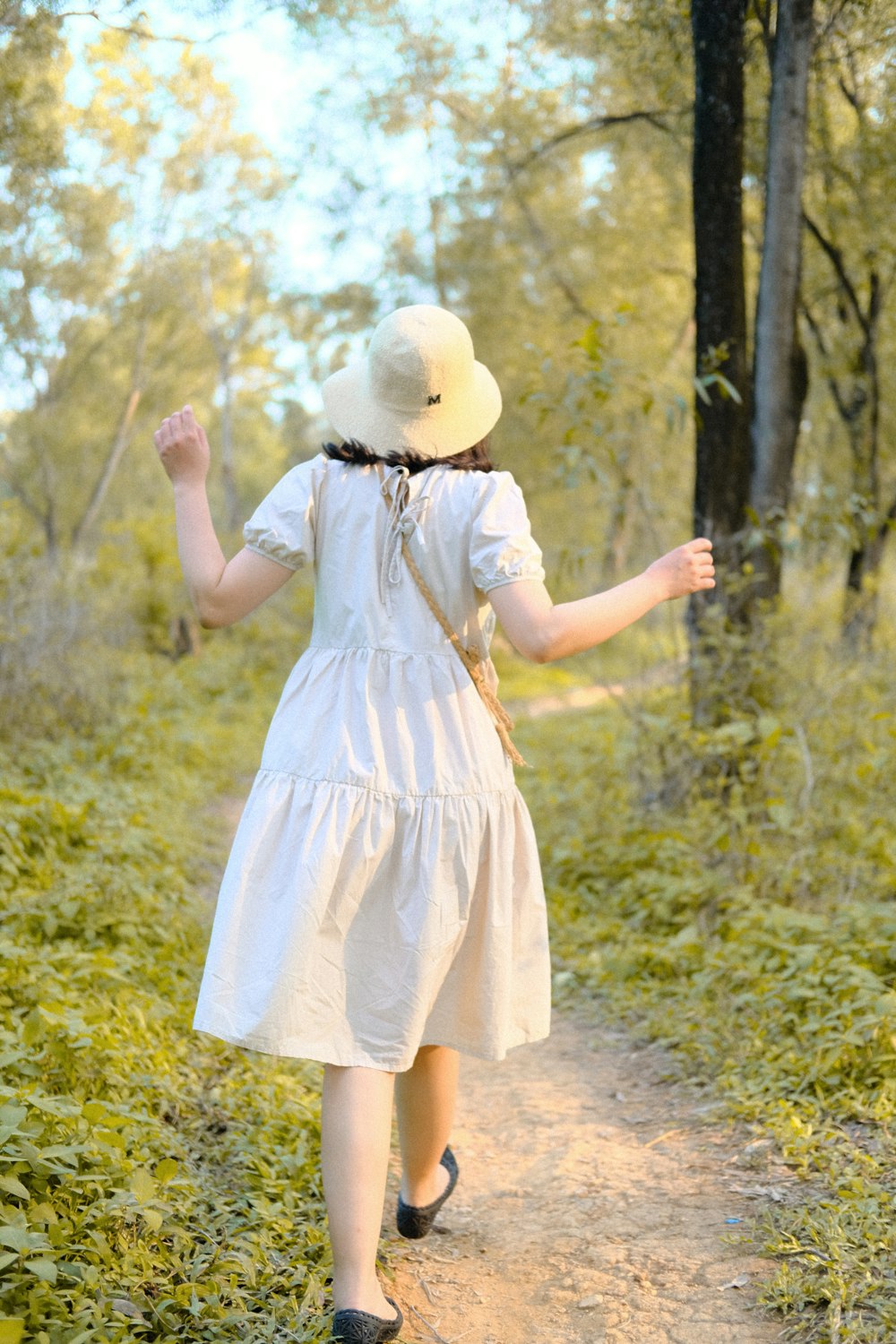 a person wearing a white dress and hat walking on a path in the woods