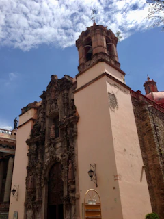 Close-up of intricate stone carvings on a mission bell tower under a bright blue sky.