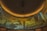 A curved panoramic display features a series of modern architectural buildings, illuminated by a warm yellow-orange light. The structures exhibit diverse architectural styles, with geometric designs and an array of windows. The setting appears to be an interior space designed for showcasing architectural imagery.