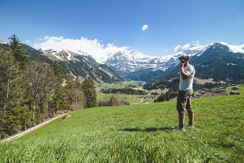 uma pessoa de pé em uma colina gramada com montanhas ao fundo