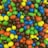 A vibrant assortment of colorful candy-coated chocolates, predominantly in green, blue, yellow, orange, red, and brown hues, scattered closely together creating a lively and fun display.